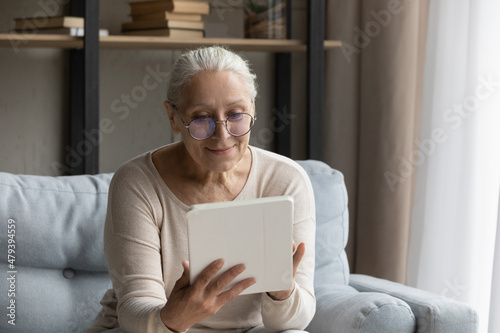 Addicted to modern technology happy old senior woman in glasses using digital touchpad gadget, web surfing information, playing games, choosing goods shopping in internet store or communicating online