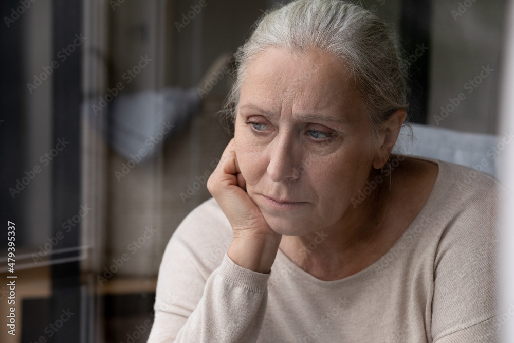 Head shot unhappy confused middle aged elderly retired woman looking in distance suffering from loneliness at home, remembering life moments, recollecting memories, thinking of psychological troubles. Head shot unhappy confused middle aged elderly retired woman looking in distance suffering from loneliness at home, remembering life moments, recollecting memories, thinking of psychological troubles.