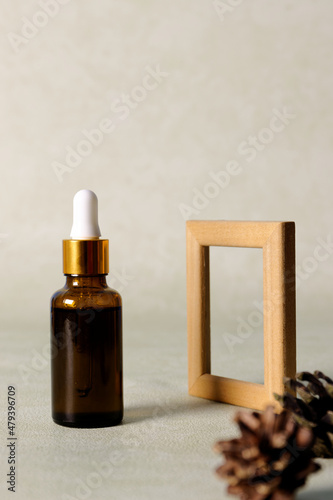Skincare serum product with pure essential oils in bottle with dropper. Wooden frame product presentation with pine cones.