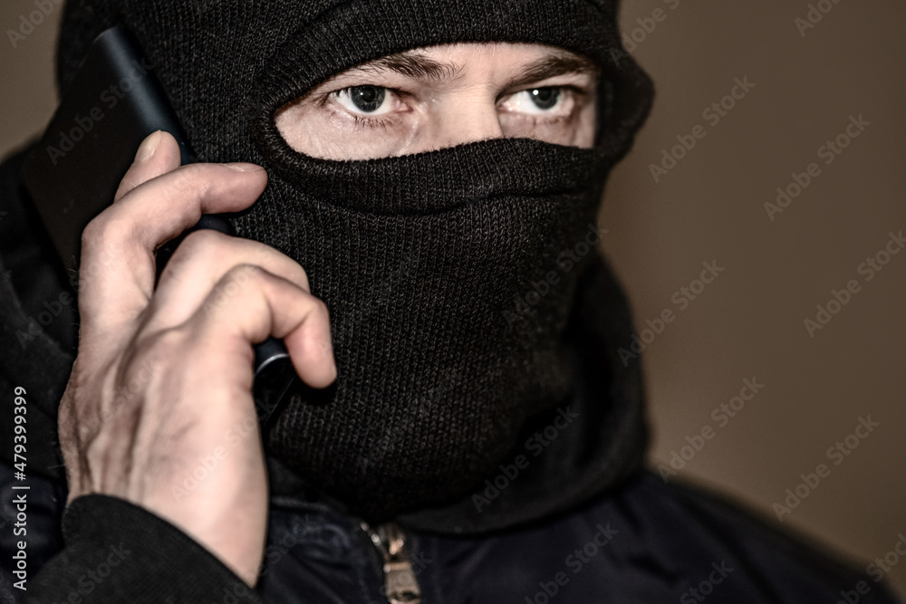 A criminal in a black balaclava and a hoodie in the dark. The concept of crime growth, robbery and fraud, unemployment and malice.