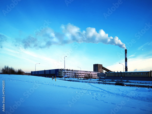 A wide view of an industrial complex with a tall pipe with smoke