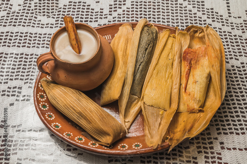 Sweet pineapple and blue tamales and red chili tamales, accompanied by white masa atole. Typical Mexican food. On a clay plate and accompanied by corn and cinnamon. photo