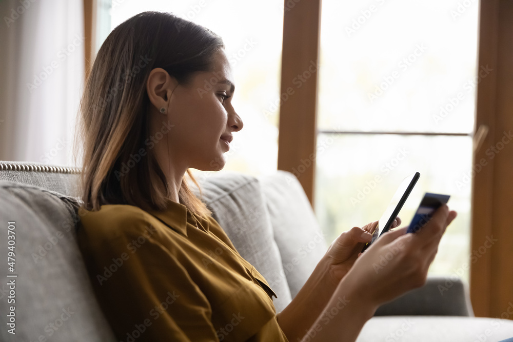 Smiling, thoughtful beautiful millennial customer woman using credit card and online shopping ecommerce app on smartphone for order, payment on Internet banking service, holding mobile phone Smiling, thoughtful beautiful millennial customer woman using credit card and online shopping ecommerce app on smartphone for order, payment on Internet banking service, holding mobile phone