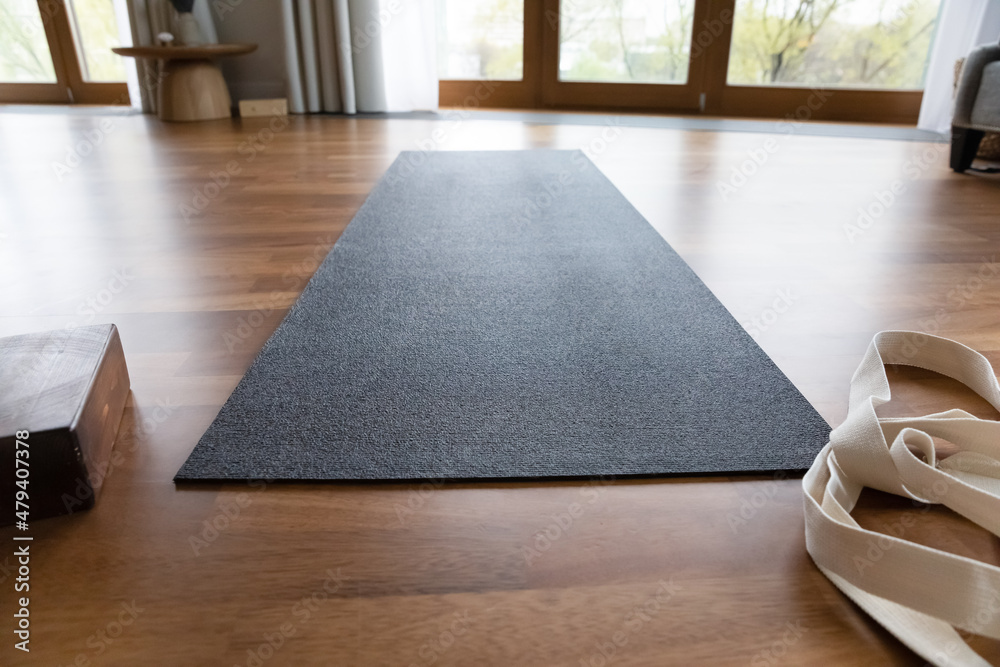 Dark grey yoga mat and strap in empty room. Sport and fitness accessory for practice, workout, exercising in home interior with parquet floor, panoramic window. Active lifestyle concept - obrazy, fototapety, plakaty 