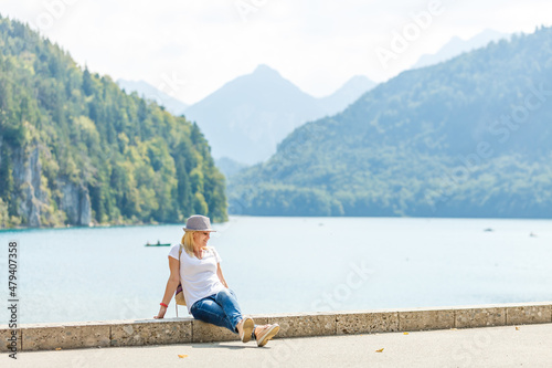 Beautiful tourist lady wearing hat and backpack enjoying stunning view on Bavarian mountains near Neuschwanstein castle in Germany. Traveling concept. Nature view