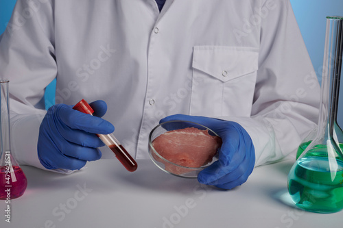 Blood test for synthetic grown meat. Doctor holds vacuum blood test tube and artificial meat in petri dish. Food control concept for fake food production. Victimless pork and beef production of GMO photo