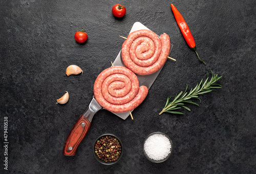 raw sausages in the form of a spiral on skewers, on a knife on a stone background