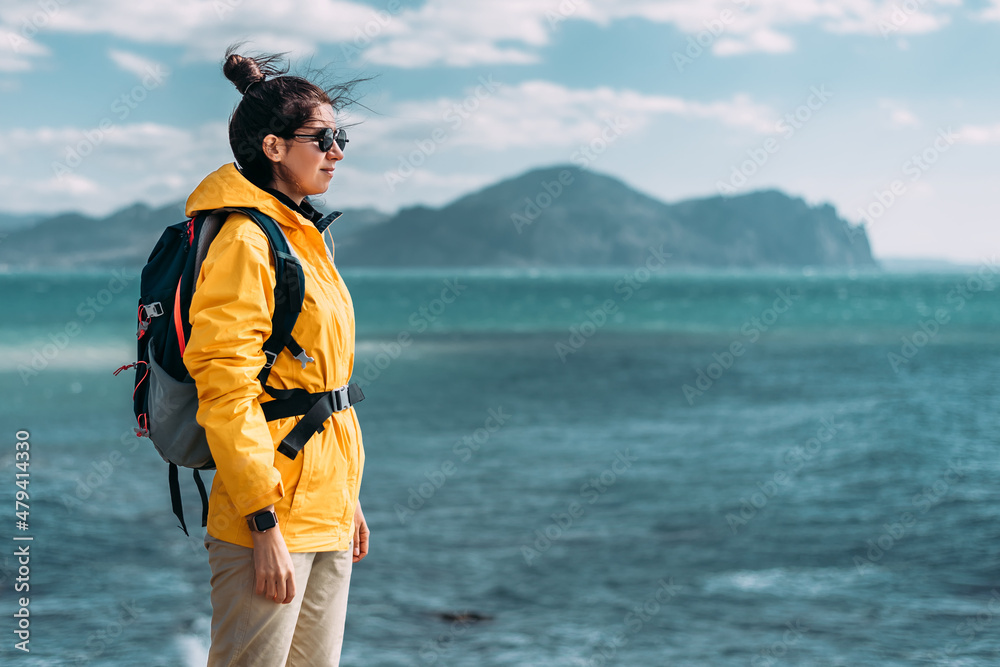 Traveler with his tourist backpack is standing against a sea background. Travel, tourism and active lifestyle concept. Portrait of a female traveler on the background of the blue sea. Copy space Traveler with his tourist backpack is standing against a sea background. Travel, tourism and active lifestyle concept. Portrait of a female traveler on the background of the blue sea. Copy space