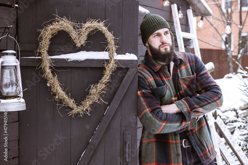 handsome bearded man in stylish winter coat stands outdoor at porch of country house, winter spirit concept, decor for valentines day
