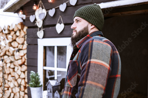 handsome bearded man in stylish winter coat stands outdoor at porch of country house, winter spirit concept, decor for valentines day