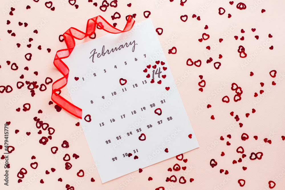 Valentine's Day. Small red hearts highlight the date February 14 on a calendar sheet and a red ribbon on a pink heart-strewn background. Top view Valentine's Day. Small red hearts highlight the date February 14 on a calendar sheet and a red ribbon on a pink heart-strewn background. Top view