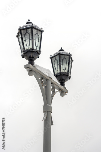Vintage lamppost covered with white snow on a gray sky.