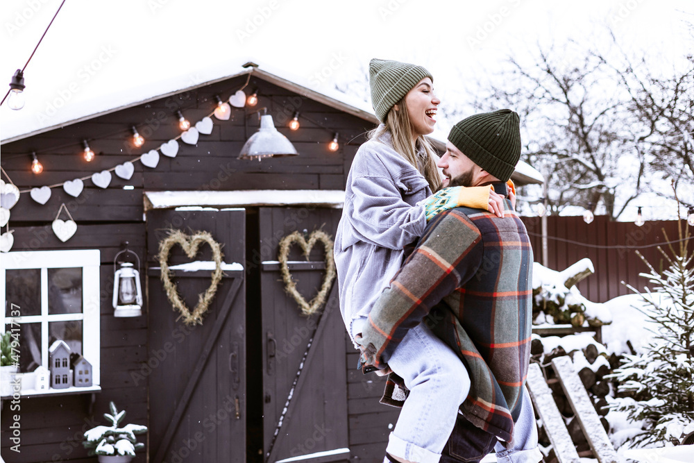 couple of young woman and man having fun in courtyard of decorated suburban house in winter, concept of Christmas and New Year vacation on farm, family love and support, Valentines Day celebration