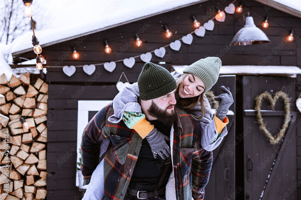 couple of young woman and man having fun in courtyard of decorated suburban house in winter, concept of Christmas and New Year vacation on farm, family love and support, Valentines Day celebration