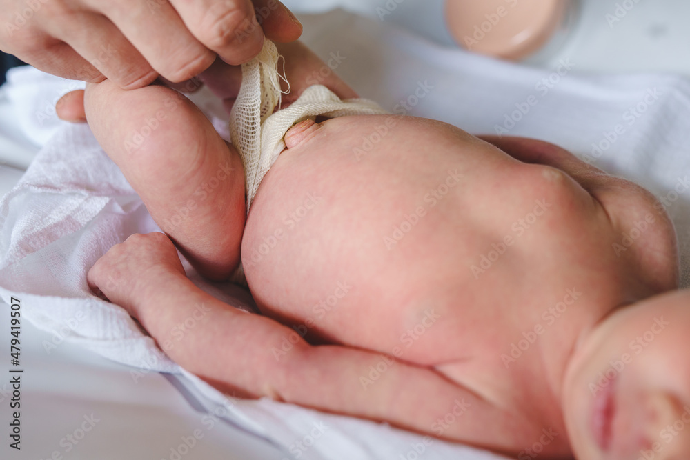 Hands of unknown man father caring for umbilical cord with clamp and bandage of newborn baby neonatal care parent clean navel of baby on bed at home