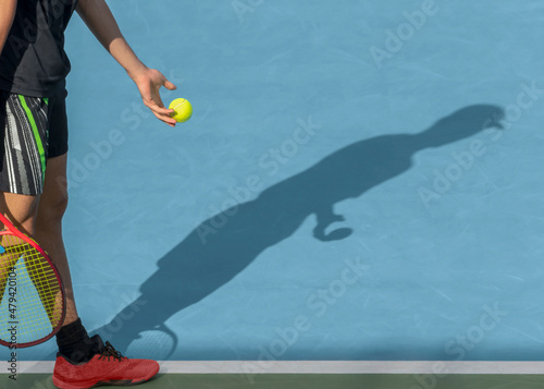Young tennis player with ball and racket performs serve while playing on red clay court. Tennis game, match, tournament concept. Sport background, shadow, copy space photo