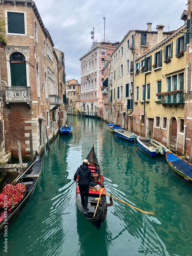 A gondolier travels along a beautiful, azure green canal in Venice surounded by the famous pink, stone buildings. Taken in winter. Venice - Italy