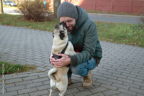 Pug dog licks human owner face. Man with his dog playing and having fun in the park. Concepts of friendship with pets and togetherness 