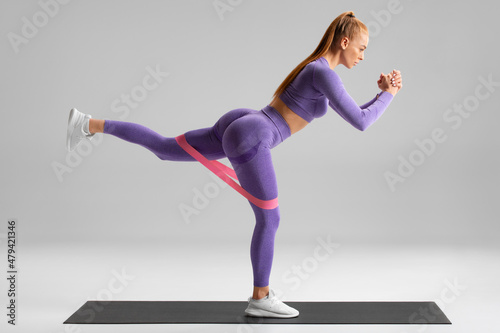 Fitness woman doing exercise for glutes with resistance band on gray background. Athletic girl working out.
