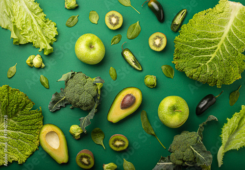 Creative layout healthy organic food concept made of green fruit and vegetables on green background flat lay: avocado, kale, broccoli, Brussels sprouts, kiwi, peppers, apple, cabbage top view
