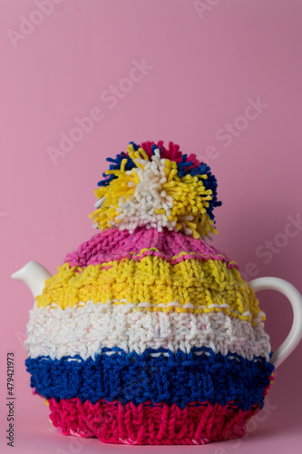 a hand knit tea cosy in bright strips on a pot of tea