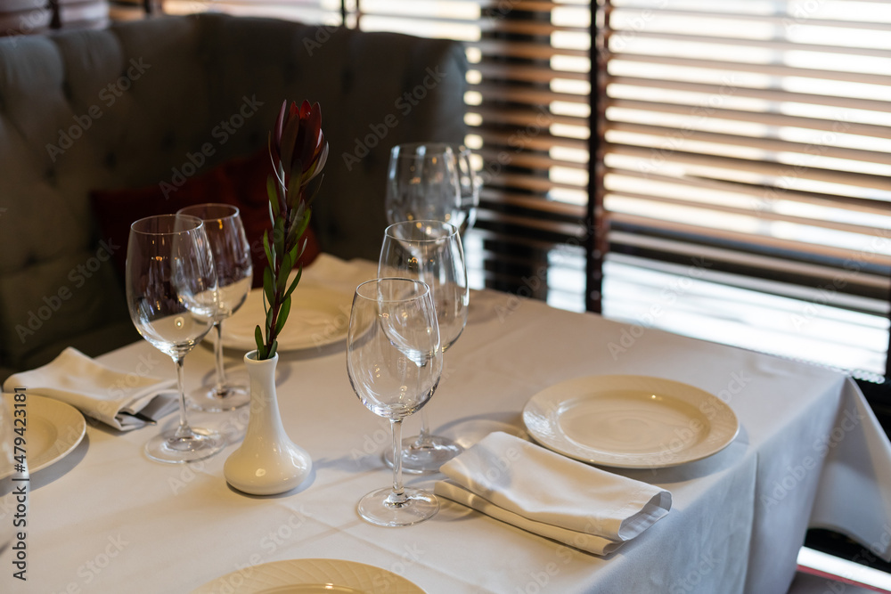 tableware Glasses, flower fork, knife served for dinner in restaurant with cozy interior.