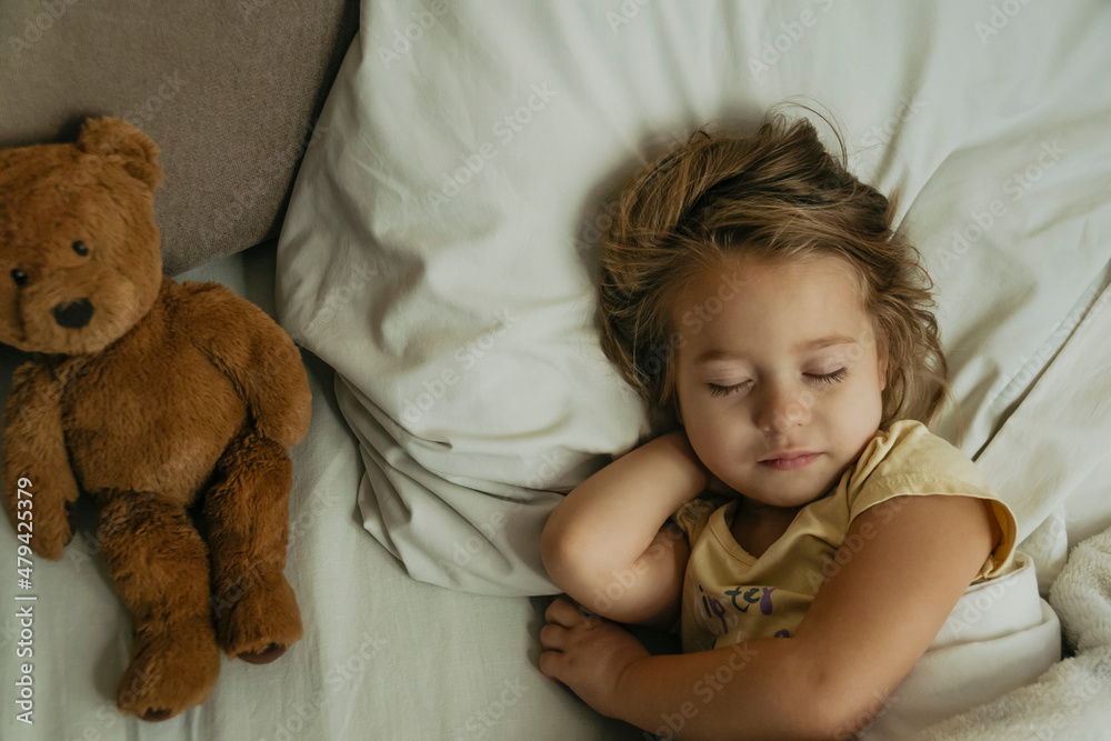 Portrait of cute little girl sleeping in bed with toy bear. Top view.