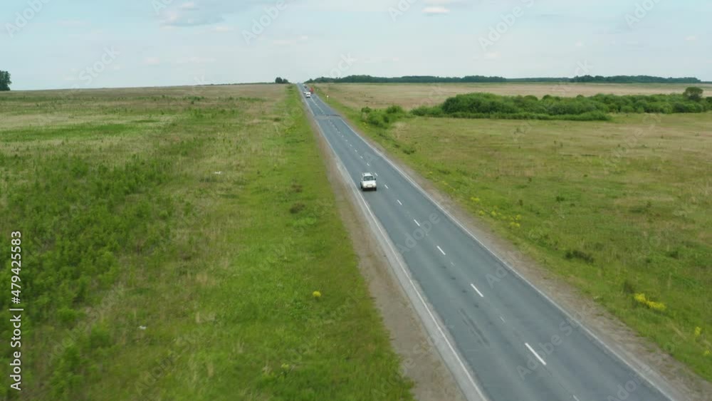 Aerial view of a car driving along the road among fields of green grass Aerial view of a car driving along the road among fields of green grass