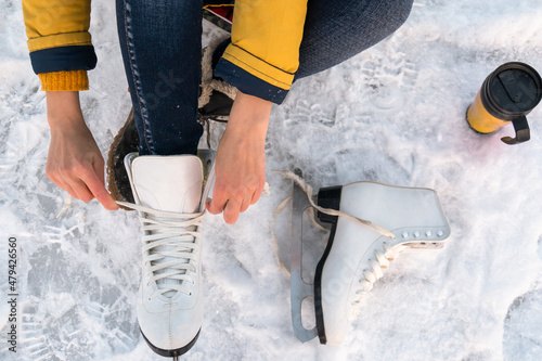 Young woman putting on ice skates. Female hands tying laces. Close up. Top view