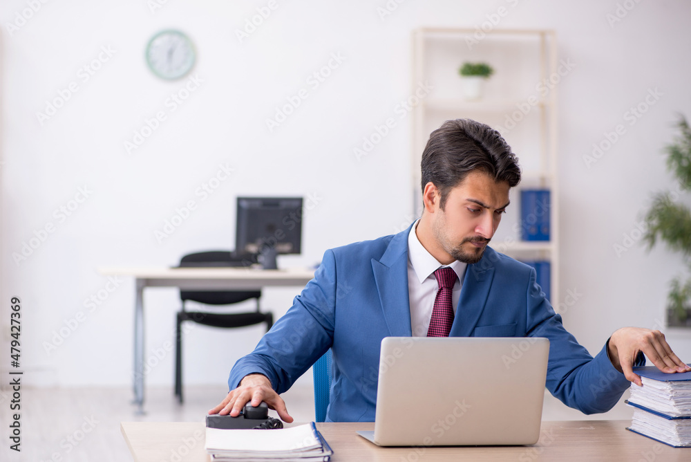 Young male employee unhappy with excessive work in the office Young male employee unhappy with excessive work in the office