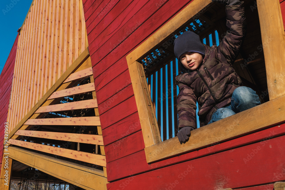 Young boy looks through window in wooden colorful construction