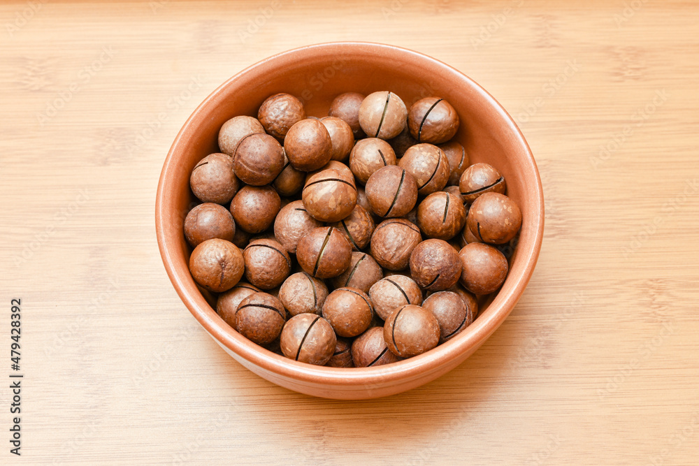 macadamia nuts in brown cup on wooden background macadamia nuts in brown cup on wooden background