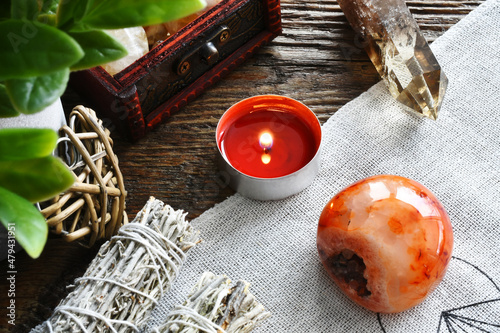 A close up image of a red carnelian crystal with a lit red candle and Smokey quartz tower on a sacred geometry grid cloth.   photo