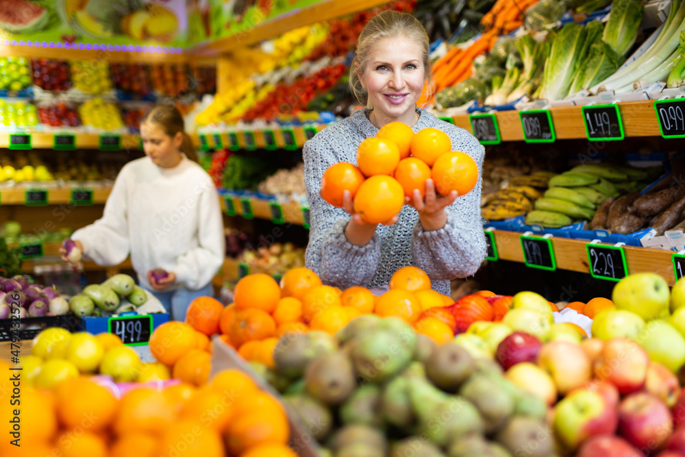 Portrait of young female choosing fresh oranges in fruit store