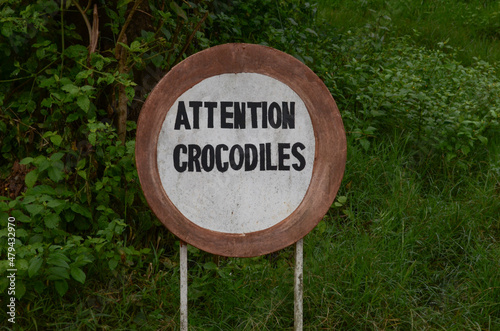A French-language sign in front of green plants in Burundi, warning of crocodiles