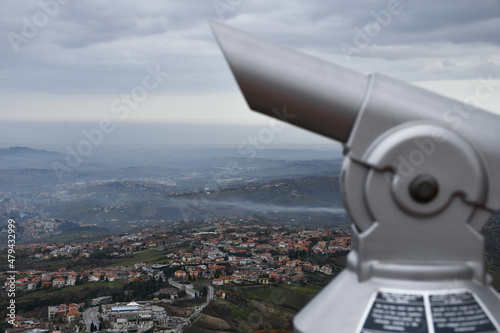 Blurry coin-operated binoculars against the backdrop of the urban area surrounding the old town of the City of San Marino on a cloudy day