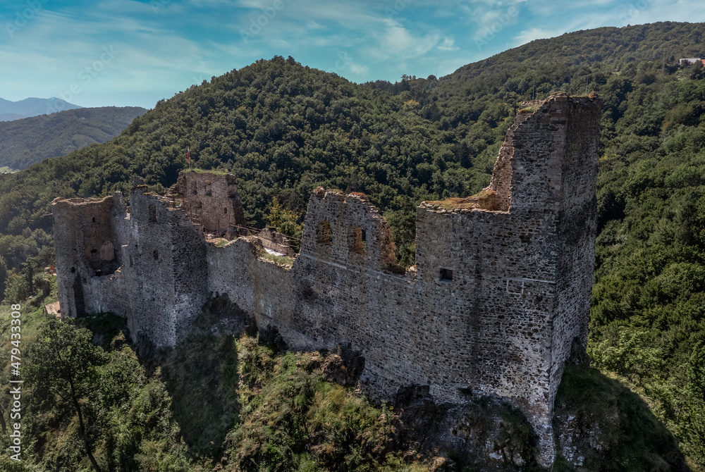 Aerial view of under restoration medieval Reviste castle above the Hron (Garam) river in Slovakia with donjon, circular gate tower, ruined gothic palace blue cloudy sky 