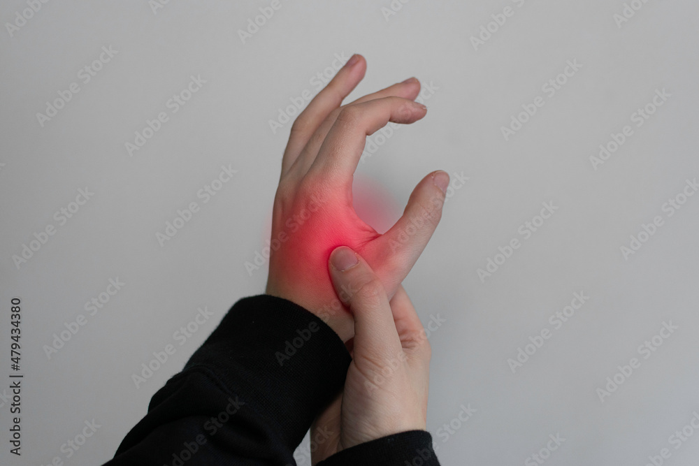 Young female suffering from pain in hands and massaging her painful hands isolated gray background. Causes of hurt include carpal tunnel syndrome, fractures, arthritis, gout attack or trigger finger - obrazy, fototapety, plakaty 
