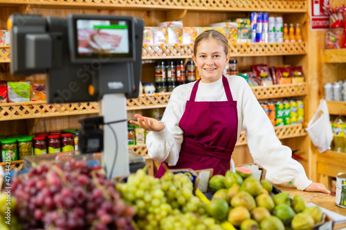 Fotografie Positive girl who works part-time as a trainee saleswoman at the checkout counte