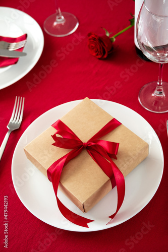 Gift box wrapped red ribbon on white plate. Romantic Valentine dinner table setting.