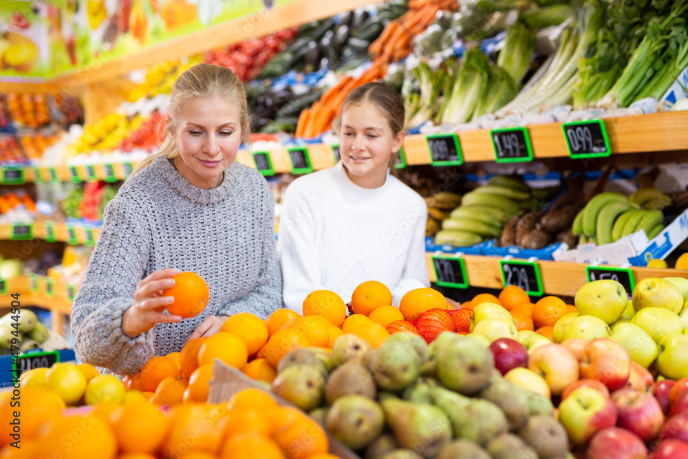 Portrait of teenage girl and her mother who buying fresh oranges at grocery shop