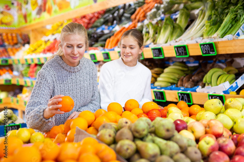 Portrait of teenage girl and her mother who buying fresh oranges at grocery shop