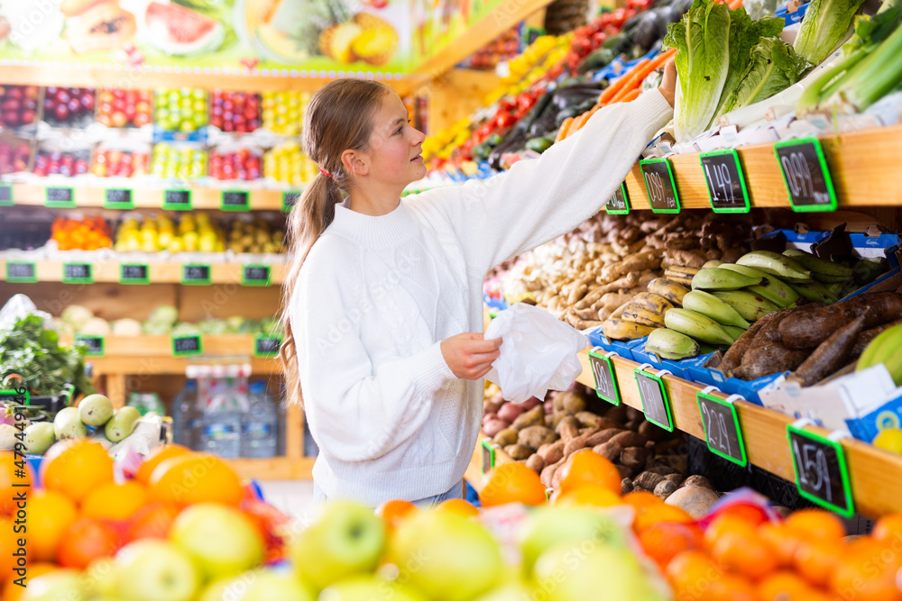 Portrait of smiling cute teen girl choosing fresh organic romaine lettuce in fruit and vegetable department of supermarket