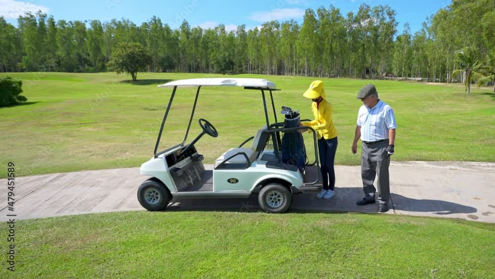 4K Asian senior man with female caddy driving golf cart together on golf course to fairway at country club. Healthy elderly male golfer walking to golfing on the green in summer sunny day 4K Asian senior man with female caddy driving golf cart together on golf course to fairway at country club. Healthy elderly male golfer walking to golfing on the green in summer sunny day