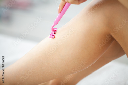 Young woman removing hair on legs with razor at bathroom.