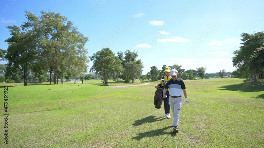 Asian man golfer walking on fairway together with female caddy on the green at golf course in sunny day. Healthy male enjoy outdoor lifestyle activity sport golfing at country club on summer vacation Asian man golfer walking on fairway together with female caddy on the green at golf course in sunny day. Healthy male enjoy outdoor lifestyle activity sport golfing at country club on summer vacation