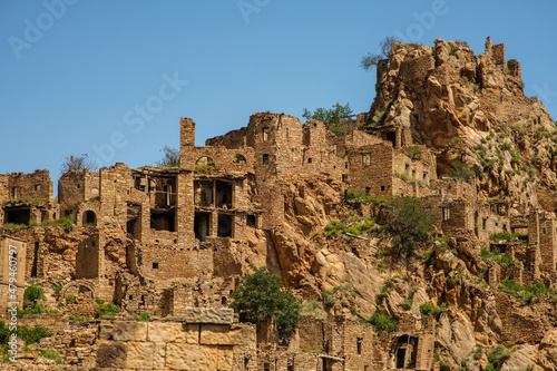 Abandoned houses of the ancient village of Gamsutl with destroyed stone walls of a building on the top of a mountain peak against the background of a blue sky in summer in Dagestan, Russia