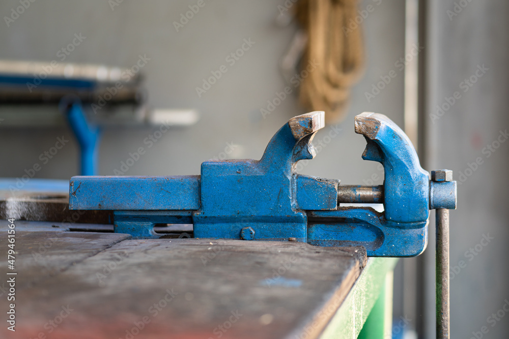An iron vise grip on workbench table at the garage repair shop. Industrial equipment object photo. Close-up and selective focus. An iron vise grip on workbench table at the garage repair shop. Industrial equipment object photo. Close-up and selective focus.