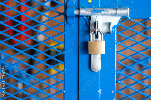 Fototapeta A key padlock is locking on metal fence gate knob of the hand tool storage box (as blurred backgroung)