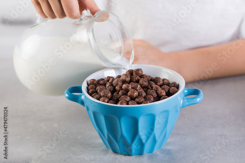 A child pours milk from a jug into a bowl of chocolate flakes. Breakfast concept